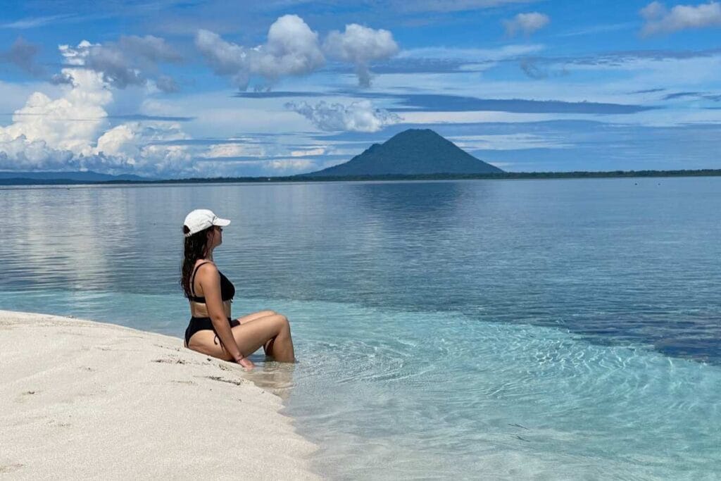Girl on sandbank between Bunaken and Nain Island with volcano view.
